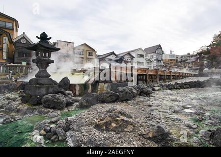 Weitblick auf das fließende schwefelhaltige Wasser und die Steinlaterne am Heißwasserfeld (Yubatake) im Kusatsu Onsen Thermalbad in Gunma, Japan, Stockfoto