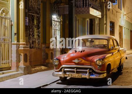 Eine abendliche Straßenszene in Havanna, Kuba mit einem klassischen Amerikanischen Auto unter Straßenlaterne. Als ein eigenes Auto benutzt, da es kein Taxi Aufkleber auf dem Bildschirm. Stockfoto