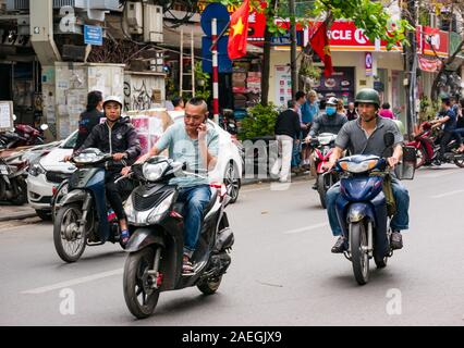 Mann auf Handy & Männer reiten Motorräder und Roller in Hanoi Street, Vietnam, Südostasien Stockfoto