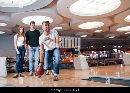 Blick auf den Menschen Werfen der Kugel. Junge fröhliche Freunde viel Spaß beim Bowling Club an den Wochenenden Stockfoto