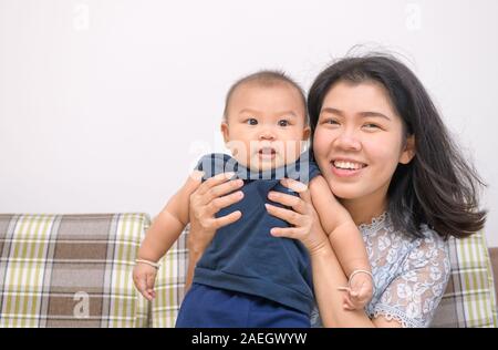 Gerne asiatische Mutter Holding Baby in den Armen und auf dem Sofa sitzen. Stockfoto