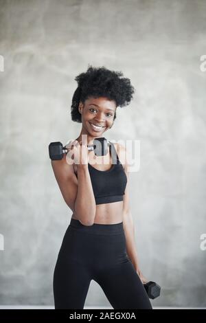 Spaß am Prozess. Studio shot der jungen Frau, die vor grauem Hintergrund mit Hanteln in den Händen steht Stockfoto