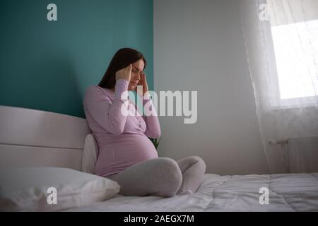 Schwangere Frau ist im Bett sitzen und mit Kopfschmerzen. Stockfoto