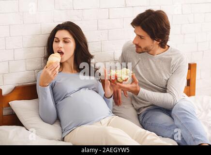 Hungrige schwangere Frau essen croissant Statt frischem Salat Stockfoto