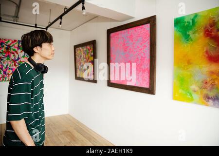 Japanische Mann mit Kopfhörer an der Abstrakten Malerei in eine Kunstgalerie. Stockfoto