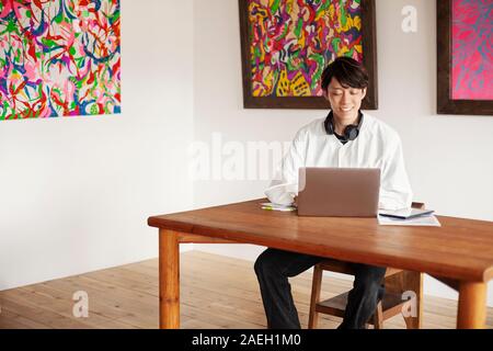 Japanischer Mann standortwahl an einem Tisch in einer Kunstgalerie, Laptop Computer. Stockfoto