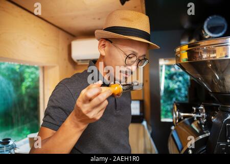 Japanische Mann mit Hut und Brille in einem Eco Cafe stehen, riechen frisch gerösteten Kaffeebohnen. Stockfoto