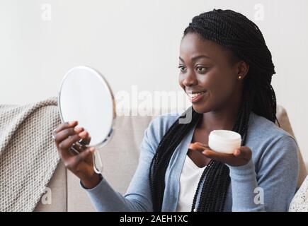 Schöne Afro Girl suchen In Vergrößerungsspiegel und Holding Cremetopf Stockfoto