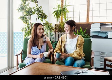 Zwei weibliche Japanische Fachleute sitzen in einem Co-Arbeitsraum, lächeln sich an. Stockfoto