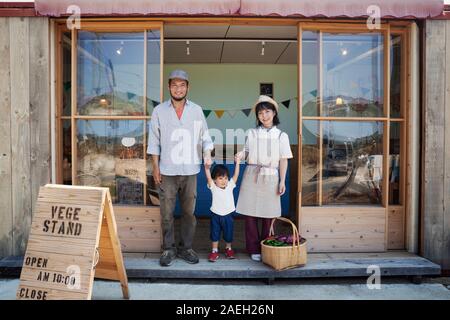 Japanischer Mann, Frau und Jungen vor einem Hofladen, Hände halten, an der Kamera schaut. Stockfoto