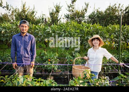 Japanische Mann mit Kappe und Frau mit Hut stehend in pflanzlichen Bereich, in die Kamera lächeln. Stockfoto