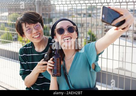 Junge japanische Mann und Frau sitzt auf einem Dach in einem urbanen Umfeld, wobei selfie mit Handy. Stockfoto