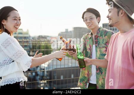 Junge Japaner, Männer und Frau, die auf einem Dach in einem urbanen Umfeld, trinken Bier. Stockfoto