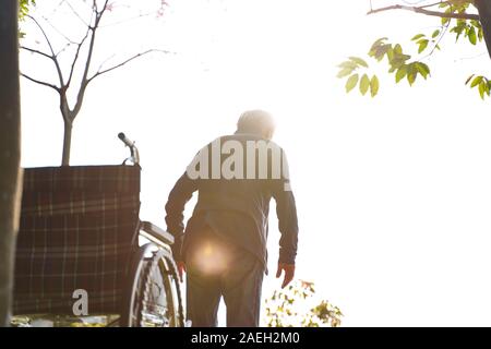 Ansicht der Rückseite des asiatischen alten Mann stehen von Rollstuhl versuchen zu laufen Stockfoto