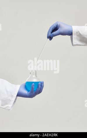 Nahaufnahme des Wissenschaftlers in der Schutzhandschuhe holding Flasche mit blauer Flüssigkeit und die Analyse von Proben auf weißem Hintergrund Stockfoto