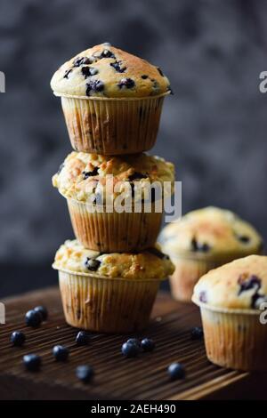 Instabiler Stapel der frisch gebackene blueberry muffins auf Eiche Schneidbrett auf dunklem Hintergrund. Low Key noch Leben mit natürlichem Licht Seitenansicht kopieren spac Stockfoto