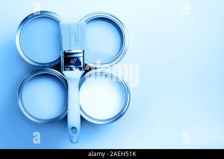 Bürste mit Holzgriff auf offenen Dosen auf Blau pastell Hintergrund. Blaue Farbe. Sanierungskonzept. Makro. Stockfoto