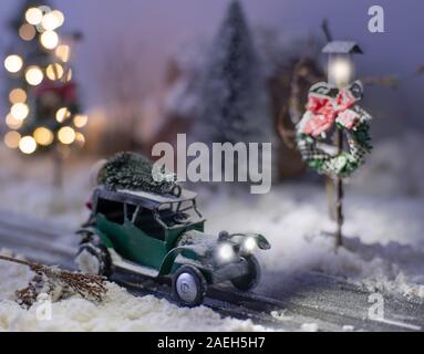 Miniatur classic car mit einem Weihnachtsbaum auf verschneiter Straße im Winter. Stockfoto