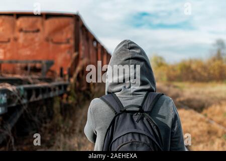 Obdachlose Frau mit Rucksack Entfliehen, Rückansicht der weiblichen Fuß unter verlassenen Waggons und veraltete Eisenbahn Stockfoto