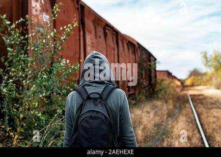 Obdachlose Frau mit Rucksack Entfliehen, Rückansicht der weiblichen Fuß unter verlassenen Waggons und veraltete Eisenbahn Stockfoto