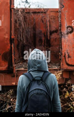 Obdachlose Frau mit Rucksack Entfliehen, Rückansicht der weiblichen Fuß unter verlassenen Waggons und veraltete Eisenbahn Stockfoto