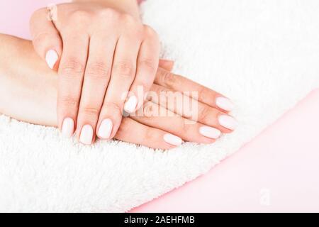 Der weibliche Hände mit klassischen Pastelltönen Maniküre auf weißen Handtuch rosa Hintergrund. Beauty Salon. Stockfoto