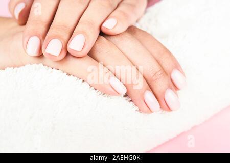 Der weibliche Hände mit klassischen Pastelltönen Maniküre auf weißen Handtuch rosa Hintergrund. Beauty Salon. Stockfoto