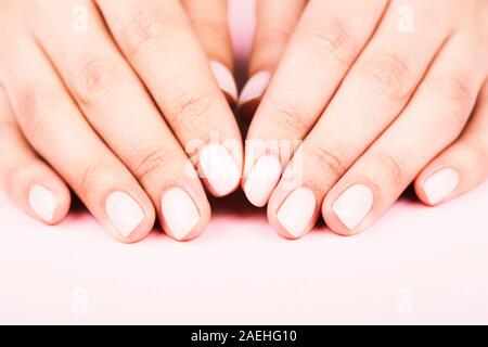 Der weibliche Hände mit klassischen Pastelltönen Maniküre auf rosa Hintergrund. Beauty Salon. Stockfoto