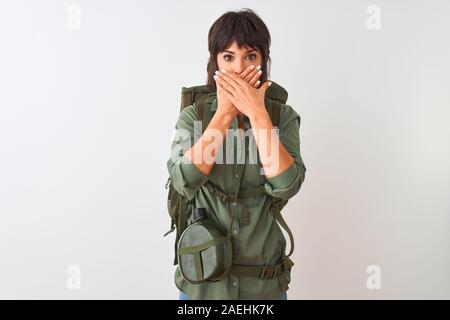 Schöne Wanderer Frau mit Rucksack und Wasser Kantine über isoliert weißer Hintergrund schockiert über den Mund mit Händen für Fehler. Geheime Konzept. Stockfoto