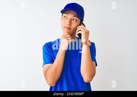 Chinesische deliveryman tragen Cap auf dem Smartphone über isoliert weißer Hintergrund ernstes Gesicht denken über Frage, sehr verworrene Vorstellung Stockfoto