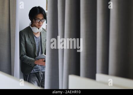 Asiatische junge Mann in Brillen und mit Kopfhörern besetzt ein Buch lesen Stockfoto