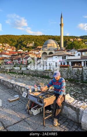Heiße Kastanien Anbieter durch die bistrica Fluss mit der Altstadt von Prizren und der Sinan Pascha Moschee im Hintergrund. im Kosovo, zentralen Balkan. Stockfoto