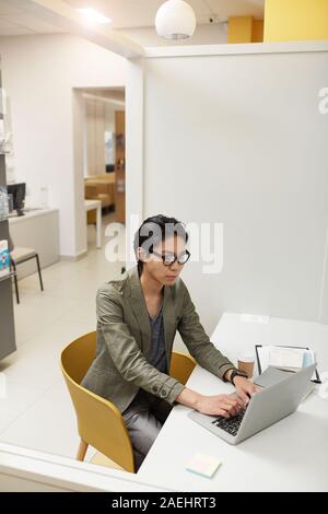 Asiatische junge Manager in Brillen am Tisch sitzen und mit Laptop, die er online auf die Arbeit im Büro Stockfoto