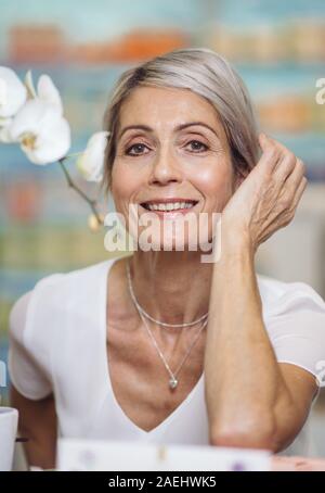 67-jährige Frau sitzt und halten ihre Hand in der Nähe von ihr Gesicht Stockfoto