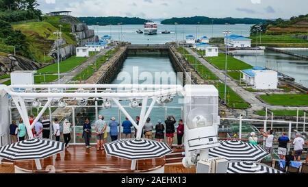 Anzeigen von Fahrgästen auf der Rückseite eines Luxus Kreuzfahrtschiff Kreuzung Agua Clara Schlösser mit einem Containerschiff warten die Schlösser als Hintergrund eingeben Stockfoto