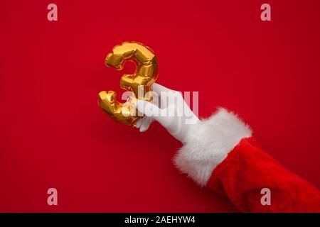 12 Tage von Weihnachten. Santa Hände halten 3. tag Ballon auf rotem Hintergrund Stockfoto