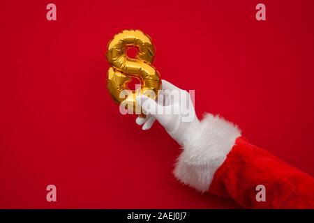 12 Tage von Weihnachten. Santa Hände halten 8 Tag Ballon auf rotem Hintergrund Stockfoto