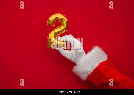 12 Tage von Weihnachten. Santa Hände halten 2 Tag Ballon auf rotem Hintergrund Stockfoto