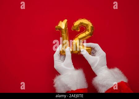 12 Tage von Weihnachten. Santa Hände halten 12. Tag Ballon auf rotem Hintergrund Stockfoto