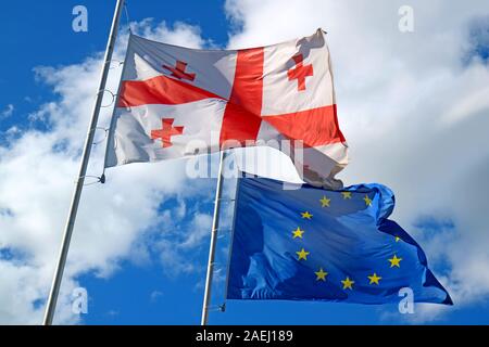 Georgische Flagge und EU-Flagge Schwenkten an sonnigen blauen Himmel Stockfoto