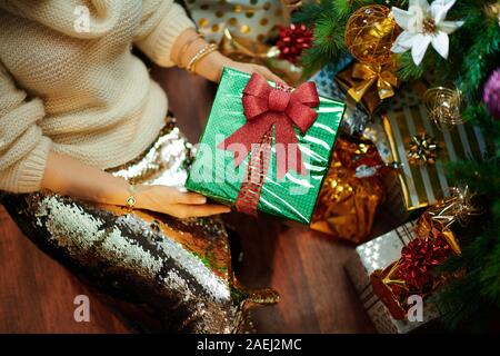 Nahaufnahme auf junge Frau in Gold Pailletten Rock und weißen Pullover unter dem geschmückten Weihnachtsbaum in der Nähe des heutigen Boxen übersicht Weihnachtsgeschenk. Stockfoto