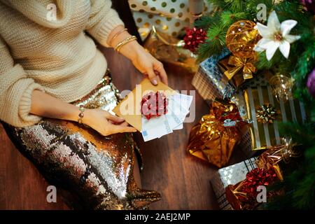 Nahaufnahme auf moderne 40 Jahre alte Hausfrau in Gold Pailletten Rock und weißen Pullover unter dem geschmückten Weihnachtsbaum in der Nähe des heutigen Boxen Suchen an Weihnachten Stockfoto