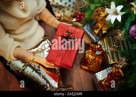 Nahaufnahme auf elegante 40-jährige Hausfrau in Gold Pailletten Rock und weißen Pullover unter dem geschmückten Weihnachtsbaum in der Nähe des heutigen Boxen mit pr Stockfoto