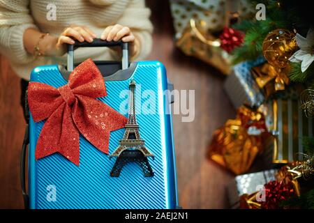 Hausfrau in Gold Pailletten Rock und weißen Pullover mit blau Reisekoffer und Eiffelturm souvenir unter dem geschmückten Weihnachtsbaum in der Nähe des heutigen Boxen Stockfoto