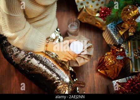 Nahaufnahme auf betonte trendy mittleren Alter Hausfrau in Gold Pailletten Rock und weißen Pullover mit Glas Wasser auf den Boden unter dem geschmückten Weihnachtsbaum Nea Stockfoto