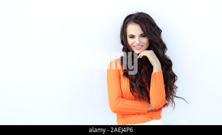 Junge schöne dunkelhaarige genießt das Leben in der Nähe eines hellen Wand in einem hellen orange Pullover. Bläst der Wind Ihr Haar, sie lächelt Stockfoto