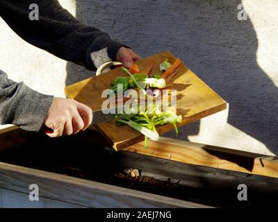 Ökologie Kompost versorgen - Küche das Recycling von Abfällen im Hinterhof Komposter. Der Mann wirft übrig gebliebene Gemüse aus dem Schneidebrett. Ökologisch fri Stockfoto