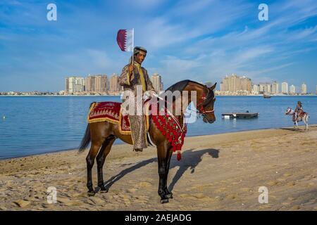 Ein katarischer Mann, der ein Pferd reitet und die Flagge von Katar trägt, in Katara Beach Doha, Katar, der den nationalen Tag von Katar feiert Stockfoto