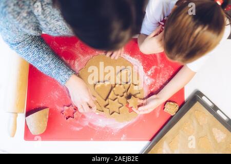 Weihnachtsbäckerei. Mutter und Tochter, Lebkuchen, schneiden Cookies von Lebkuchen Teig, Ansicht von oben. Festliche Essen, Kochen, Familie Stockfoto