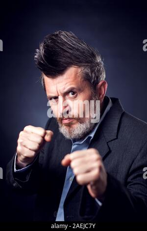 Ein Porträt von bärtigen Mann mit Irokesen tragen Anzug zeigt Faust Geste vor schwarzem Hintergrund. Menschen und Emotionen Konzept Stockfoto